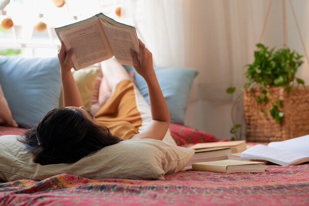 Over the head shot of brunette lying in bed reading a book