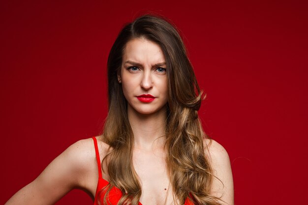 Head shot of young displeased serious female frowning on red studio background with copy space for advertising