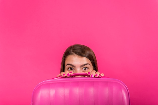 Free photo head of woman hiding behind a pink suitcase