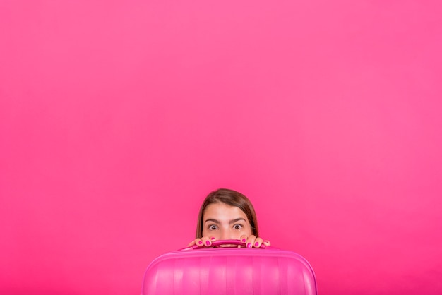 Foto gratuita testa di donna che guarda dietro la valigia rosa.