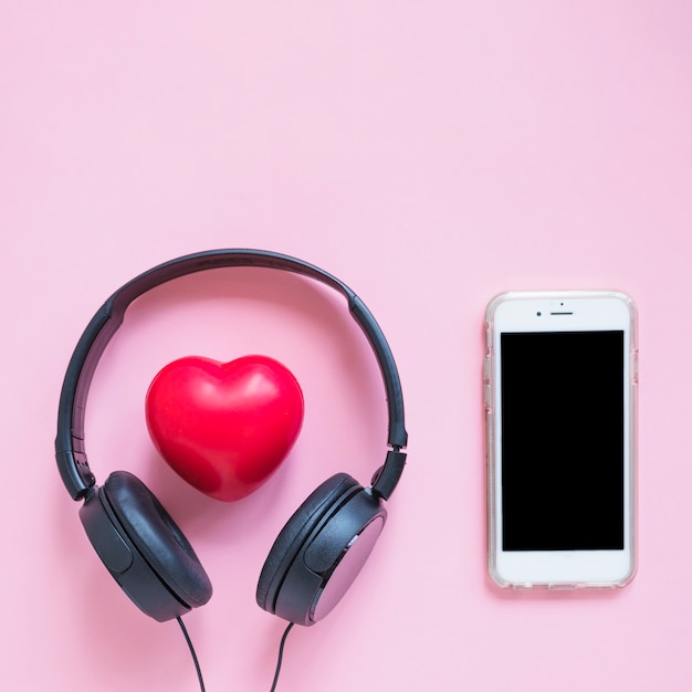 Наушники вокруг красной формы сердца и смартфона на фоне розового