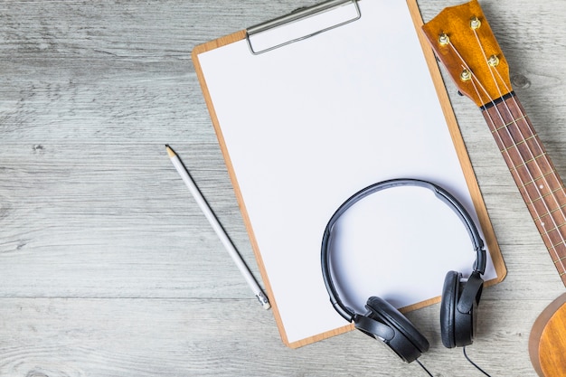 Headphone over clipboard with guitar headstock and pencil on wooden backdrop