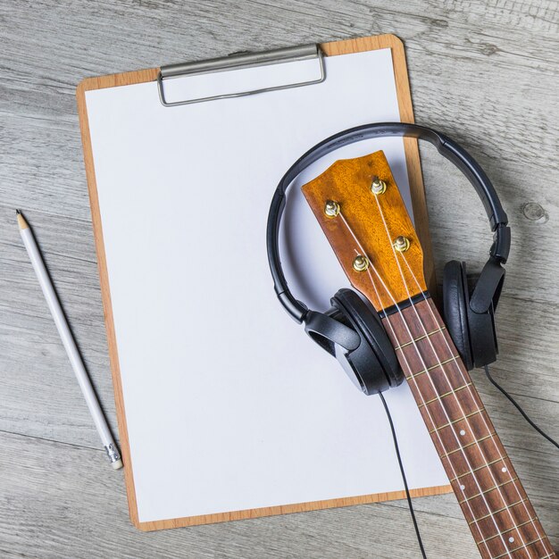 Headphone over the guitar headstock over the white paper on clipboard with pencil