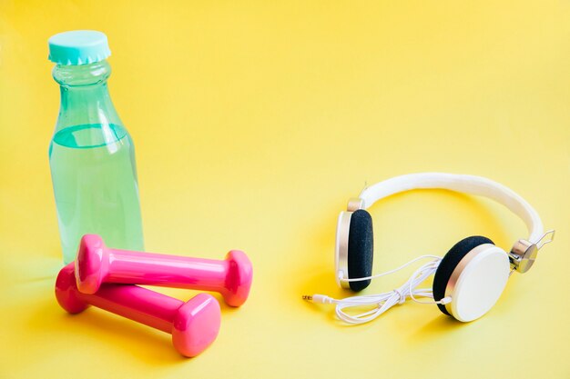 Headphones near bottle of water and dumbbells 