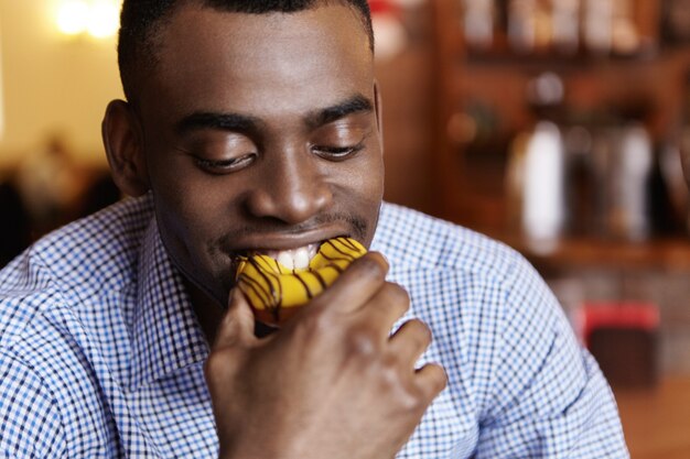 Headshot of attractive young African-American businessman biting doughnut