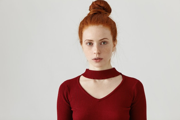 Free photo headshot of beautiful young female with freckles and ginger hair knot standing at white wall