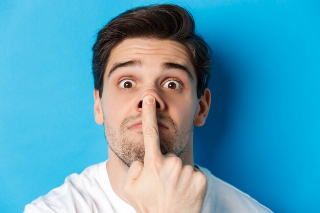 Headshot of caucasian guy making funny expressions, standing over blue background