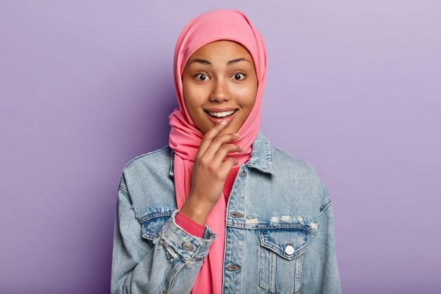 На фото веселая темнокожая мусульманка с нежной улыбкой, белыми зубами и розовым хиджабом.