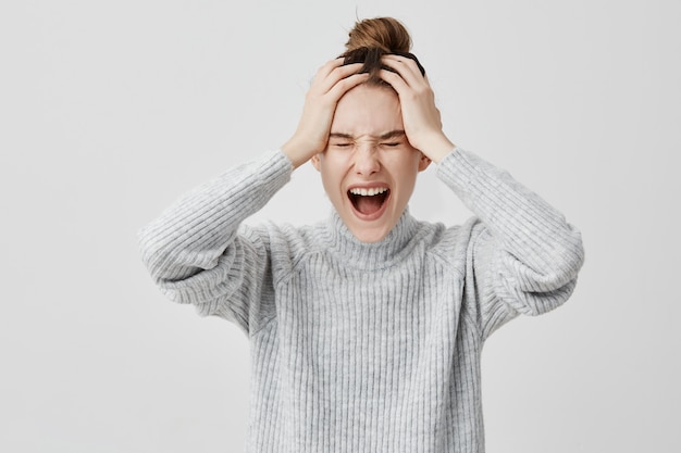 Headshot of frustrated female 30s screaming grabbing her head. Perplexed businesswoman being in shock shouting in despair having problem with work.  Emotions concept