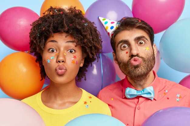 Headshot of funny young couple posing surrounded by birthday colorful balloons