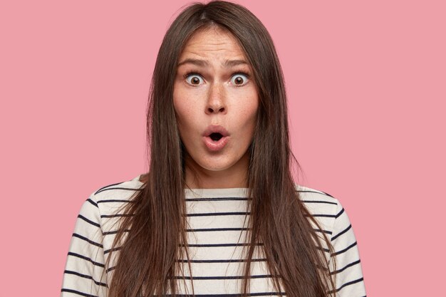 Headshot of good looking freckled girl with long straight hair, has frightened expression