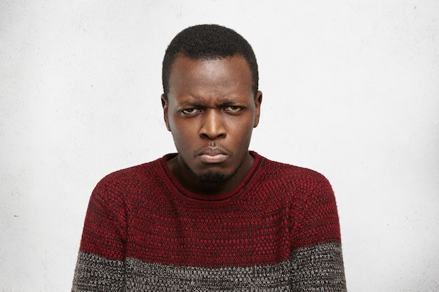 Headshot of grumpy unhappy young dark-skinned male dressed casually frowning