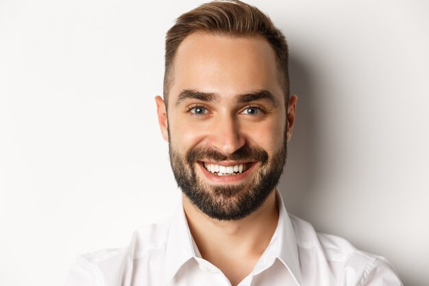 Headshot of handsome bearded man smiling, standing against white background.