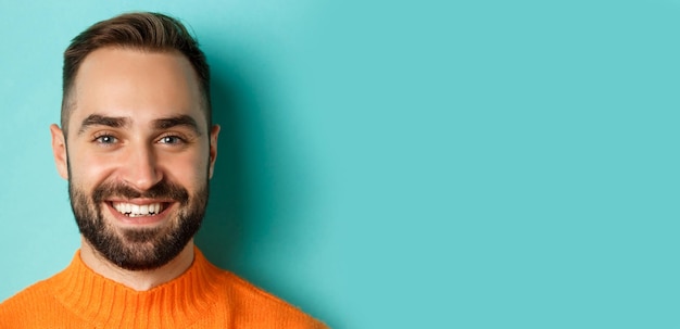 Headshot of handsome caucasian man with beard smiling happy at camera standing in orange sweater aga