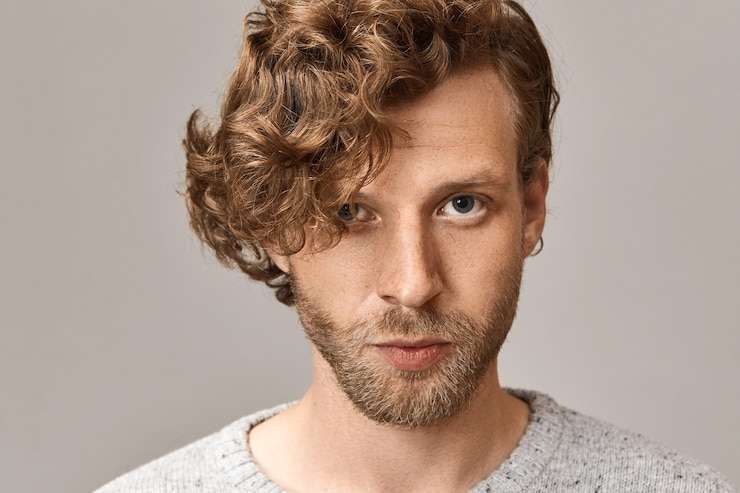 Free Photo headshot of handsome fashionable young blue eyed man with stylish ginger curls, freckles and trimmed beard with confident facial expression, wearing gray sweater and round earring