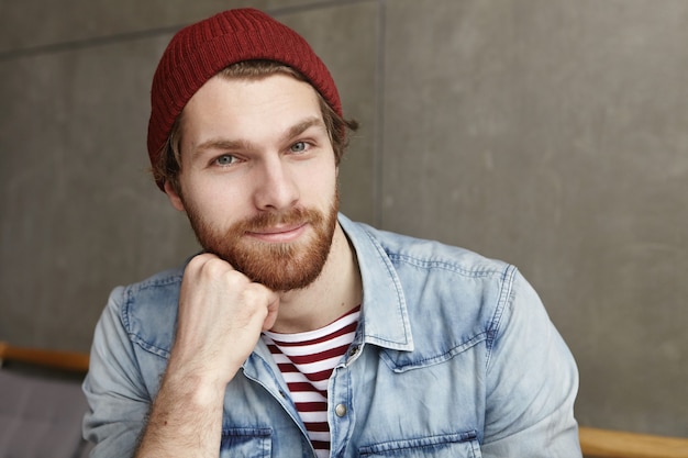 Headshot of handsome stylish young man in trendy hat and blue denim jacket over striped t-shirt