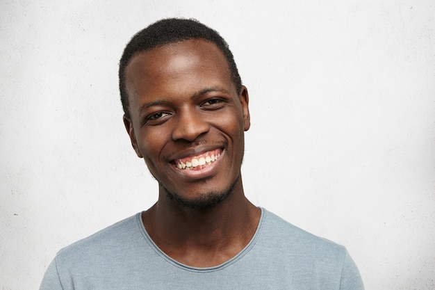 Headshot of handsome young Afro American male looking with broad friendly smile, enjoying good day and leisure time indoors. Black man feeling happy and carefree while relaxing at home