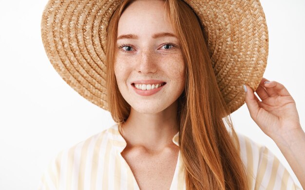 휴가를 즐기는 행복한 매력적인 빨간 머리 소녀의 얼굴 만은 광범위하게 머리에 밀짚 모자를 들고 웃고 친절한 기쁘게 표현으로 응시하고 있습니다.