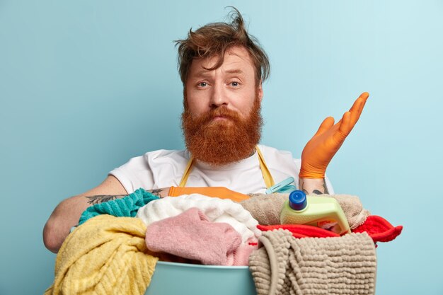 Headshot of hesitant red haired bearded man raises hand with doubt