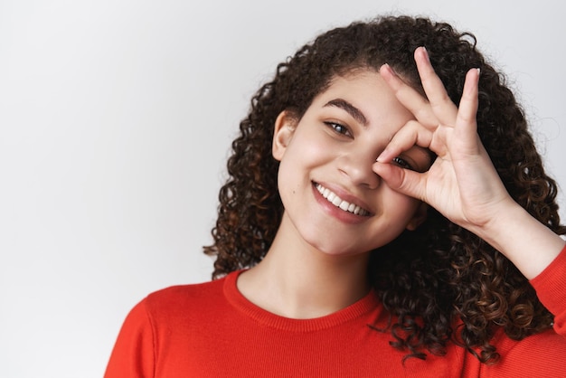 Headshot lively charismatic happy smiling toothy young attractive girl dark curly hairstyle tilting head shaking energized show okay ok perfection gesture look circle through idea grinning