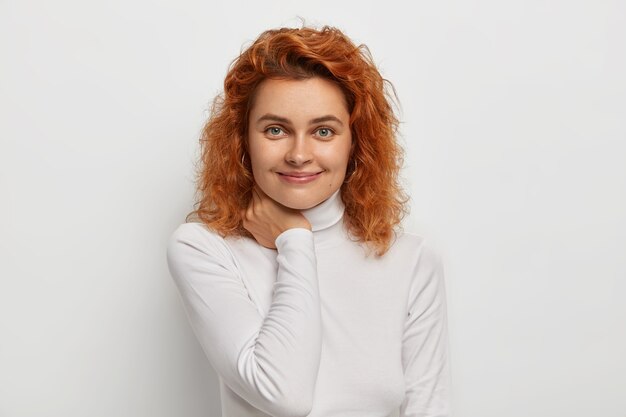 Free photo headshot of pleasant looking ginger woman with satisfied expression, touches neck, has natural beauty