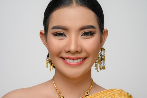 Headshot, portrait Beautiful Asian woman in traditional Thai dress costume smile and pose gracefully on white wall