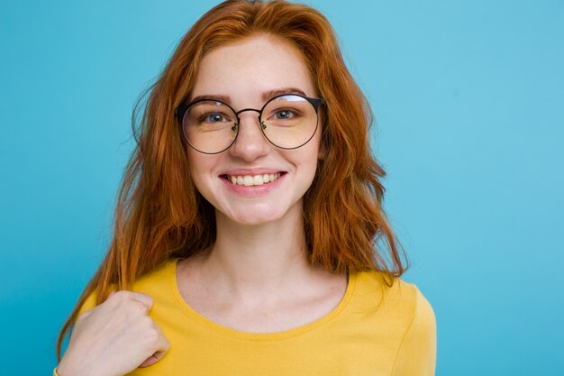 Headshot Portrait of happy ginger red hair girl with freckles smiling looking at camera. Pastel blue background. Copy Space.