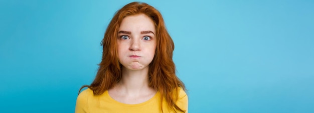 Ritratto in primo piano di una ragazza felice con i capelli rossi di zenzero con una faccia buffa che guarda la fotocamera sfondo blu pastello