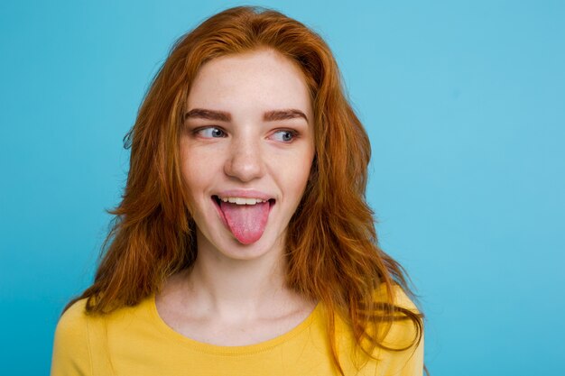 Headshot Portrait of happy ginger red hair girl with funny face looking at camera. Pastel blue background. Copy Space.