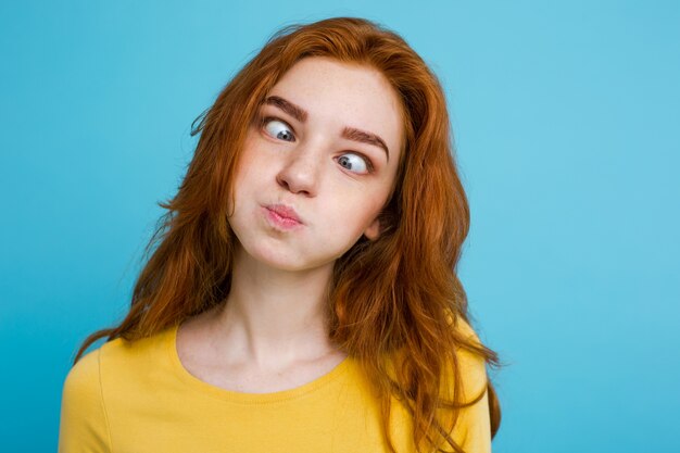 Headshot Portrait of happy ginger red hair girl with funny face looking at camera. Pastel blue background. Copy Space.