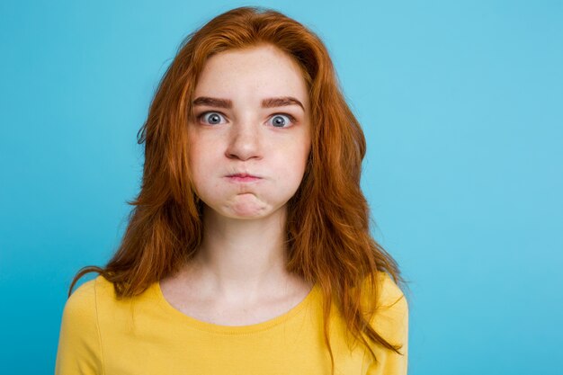 Headshot Portrait of happy ginger red hair girl with funny face looking at camera. Pastel blue background. Copy Space.