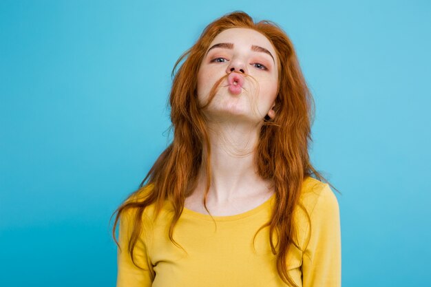 Headshot Portrait of happy ginger red hair girl with funny face looking at camera. Pastel blue background. Copy Space.