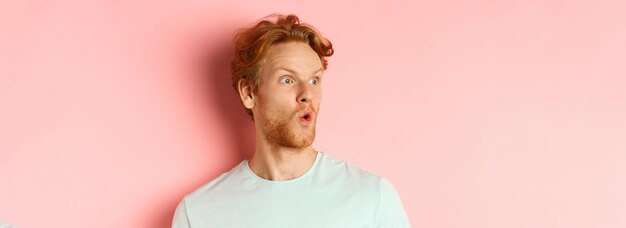 Headshot portrait of surprised redhead man with beard looking left and saying wow raising eyebrows a