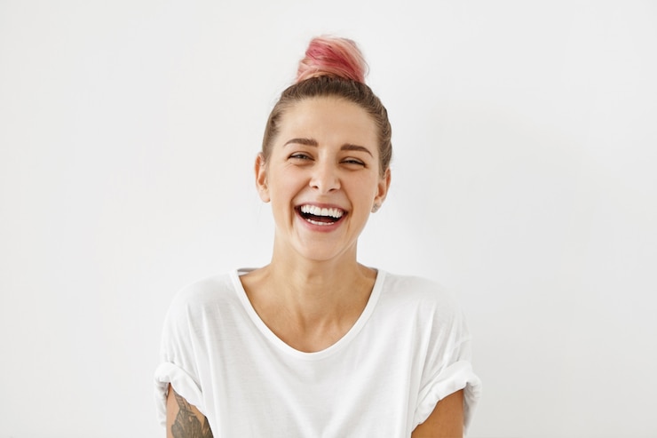 Free Photo headshot of positive emotional gorgeous young woman wearing pinkish hair bun grinning broadly, enjoying good day. beautiful woman with tattoo on arm having fun indoors, laughing at something funny