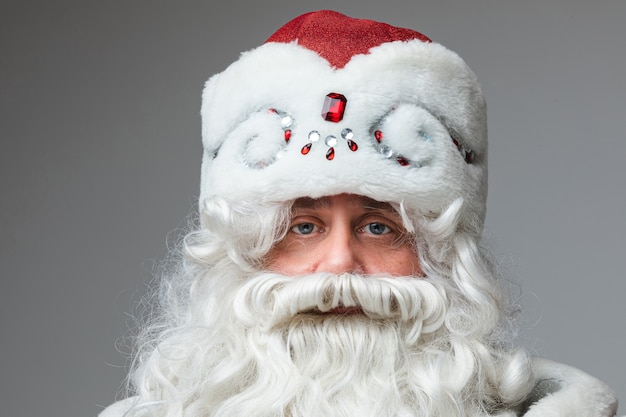 Primo piano del volto di babbo natale con cappello rosso, uomo stanco con i capelli grigi