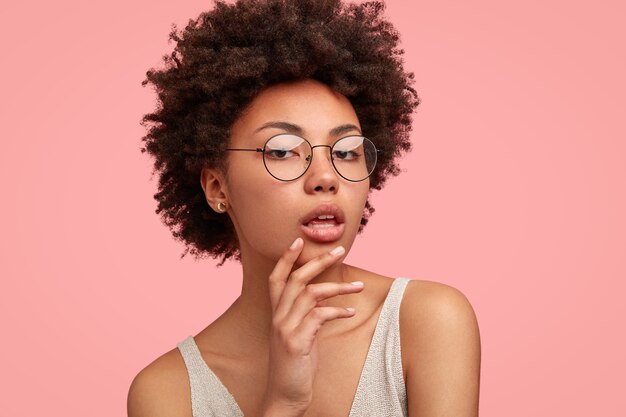 Headshot of self confident dark skinned young female keeps hand on chin