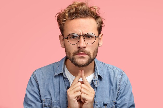 Headshot of serious intelligent young man listens something with attentive look, has scrupulous gaze