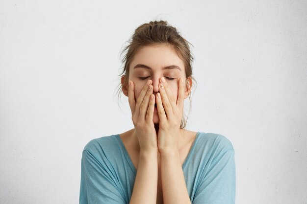 Headshot of young beautiful woman closing her eyes holding hands on chin being tired