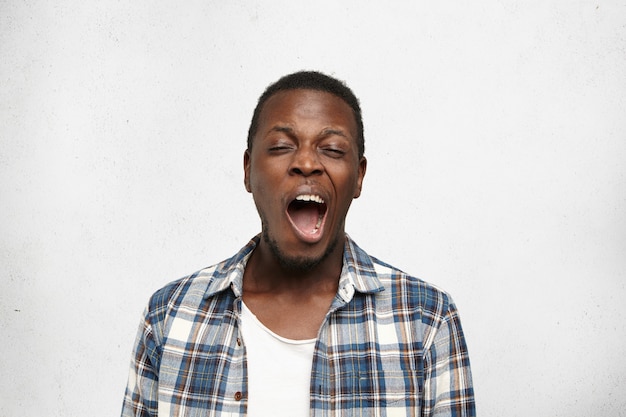 Headshot of young bored black man, yawning isolated on light background.