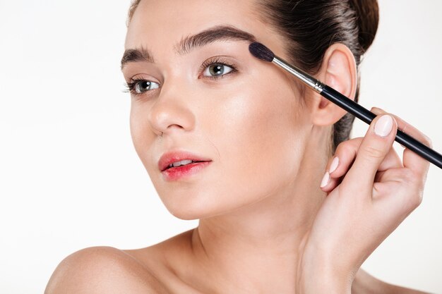 Health and beauty of glamour trendy woman with dark hair in bun applying eye shadow using brush