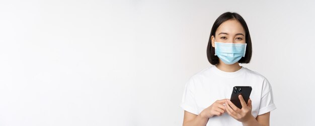 検疫で携帯電話アプリケーションを使用して医療フェイスマスクで健康とcovidコンセプトアジアの女の子