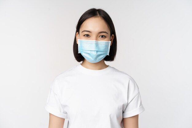 健康とcovidパンデミックの概念コロナウイルスの白い背景から身を守る幸せで自信を持って見える医療用フェイスマスクを身に着けている笑顔のアジアの女の子