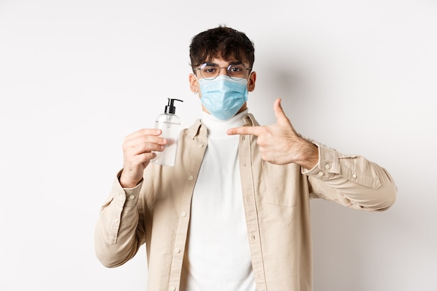 Health covid and quarantine concept cheerful young guy in face mask an glasses pointing finger at bo...