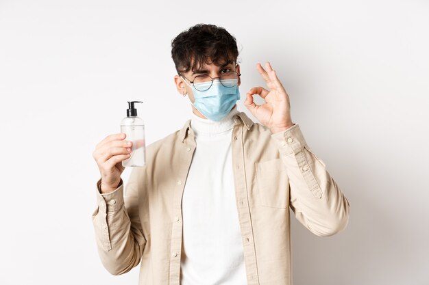 Health covid and quarantine concept portrait of natural guy in glasses and face mask showing bottle ...