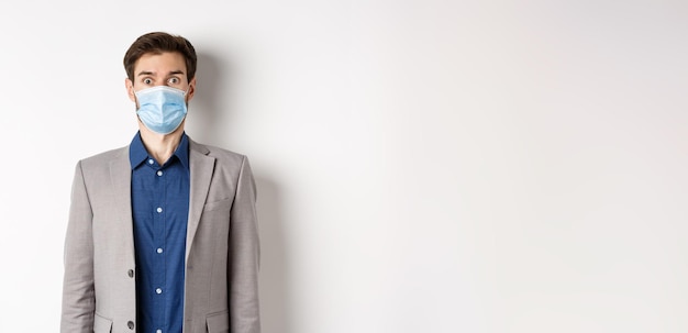 Free photo health pandemic and business concept surprised guy in suit and medical mask raising eyebrows stare s