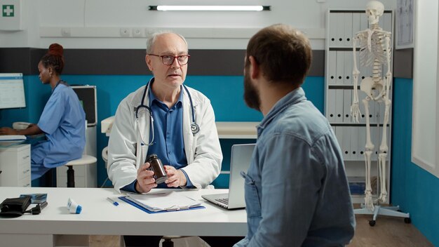 Health specialist explaining disease treatment to patient in cabinet, showing bottle of prescription medicine pills. Flask with painkillers, drugs and medication to cure health care disease.