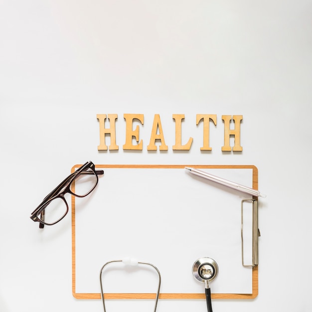 Health text near the clipboard with eyeglasses; stethoscope and pen on white background