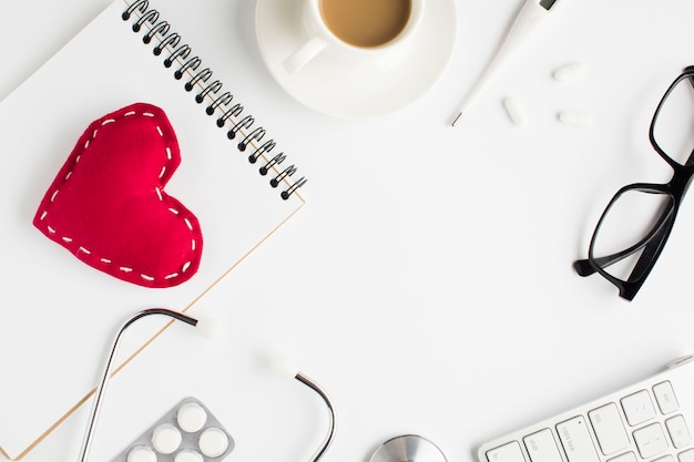 Free photo healthcare accessories with red toy heart and spiral notepad on white background