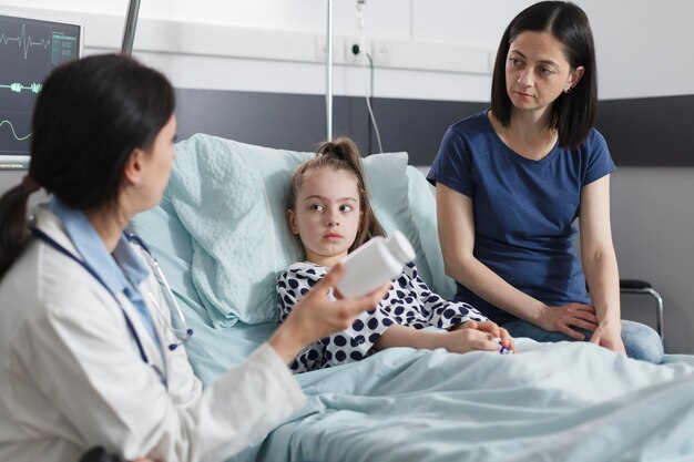 Healthcare facility clinic pediatric expert recommending ill patient girl right medicine for disease remission. Hospital pediatrist specialist talking with attentive mother about illness treatment.