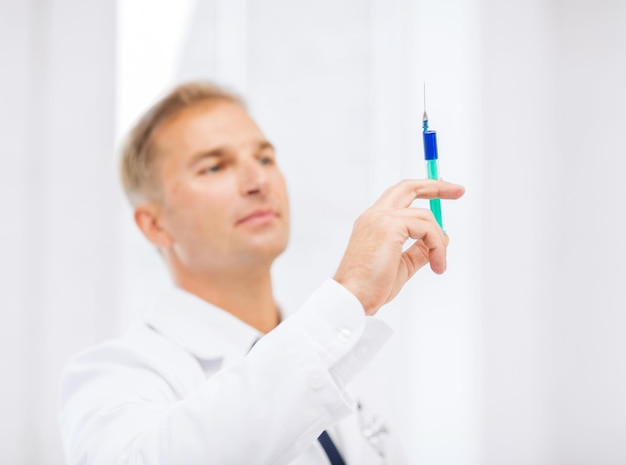 Healthcare and medical concept - male doctor holding syringe with injection